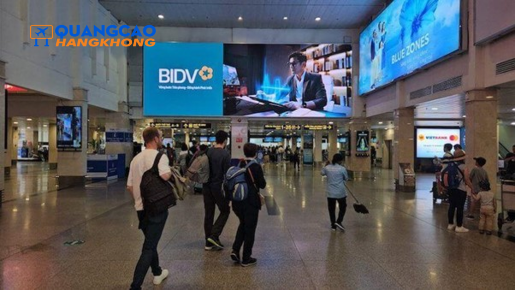 Màn hình LED cỡ lớn hiển thị quảng cáo trong sảnh nhà ga sân bay Nội Bài, hành khách di chuyển phía dưới.