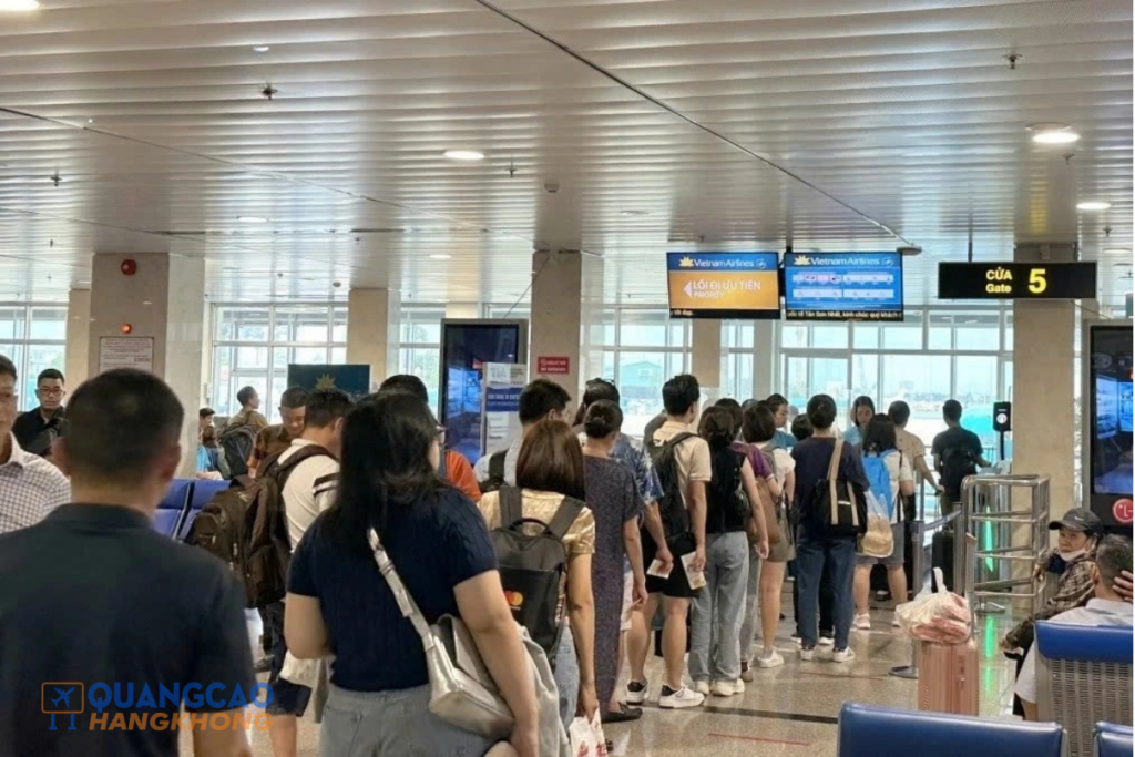 Hành khách xếp hàng tại cửa ra tàu bay (Gate 5) ở sân bay Nội Bài, phía trước là biển chỉ dẫn và màn hình thông tin chuyến bay.